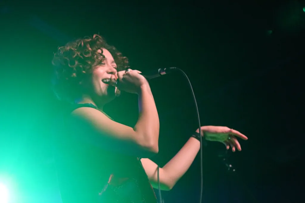 Singer performing on stage under green and pink stage lights.