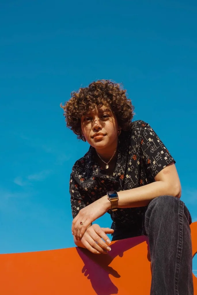 Outdoor portrait leaning on a curved orange structure against a clear blue sky.