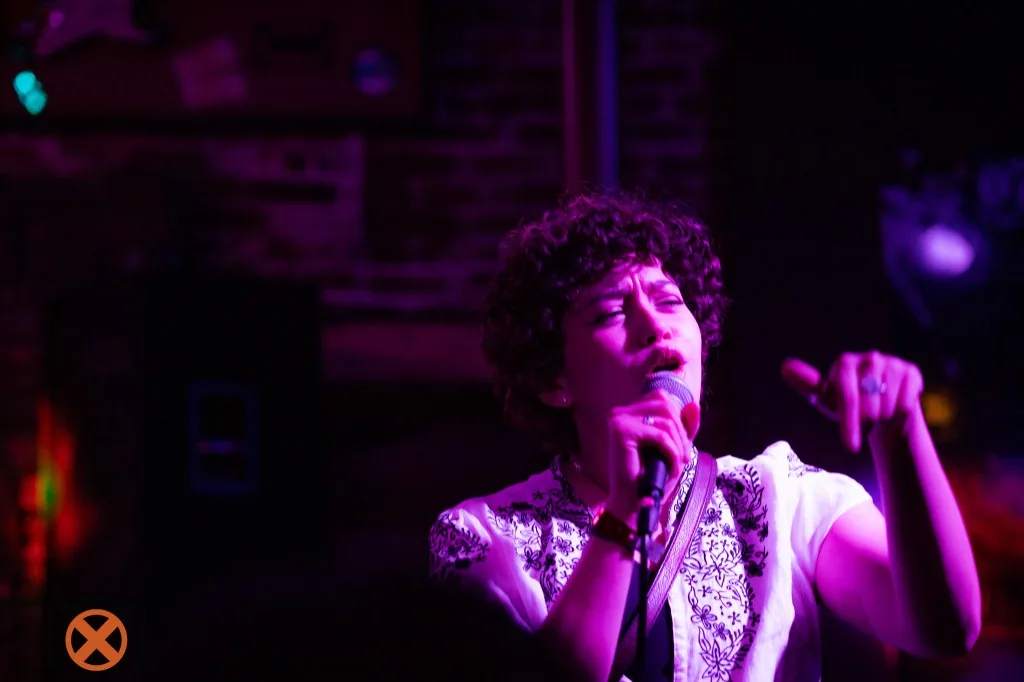 Live performance singing into a microphone under purple stage lighting.