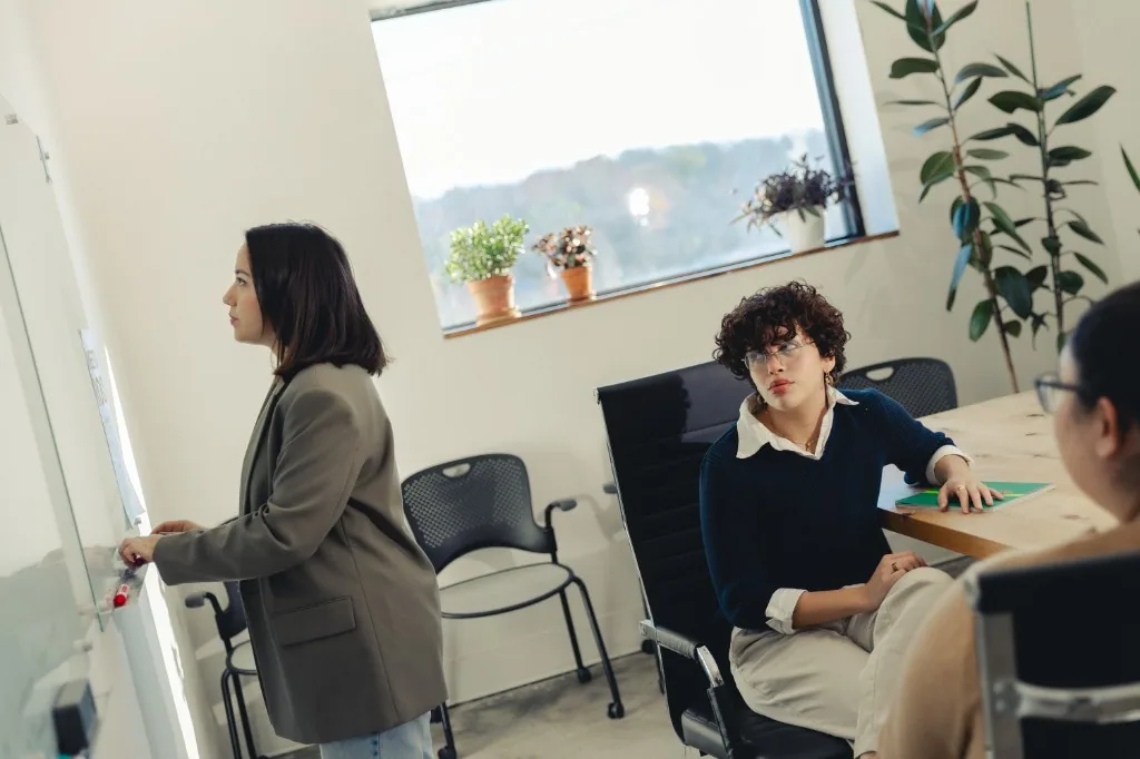 Collaborative meeting at a glass whiteboard in a bright modern office.