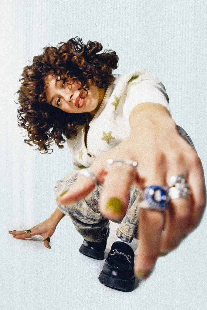 Crouched portrait in a star-patterned sweater with a hand extended toward the camera.
